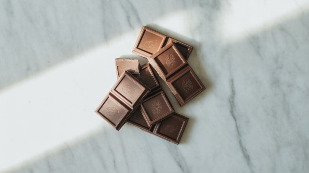 Broken dark chocolate pieces arranged aesthetically on a white marble surface.